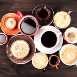 Many different cups of coffee on dark wooden table, top view.